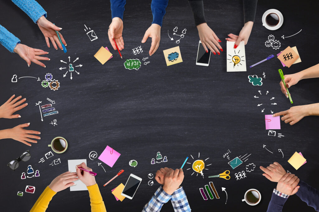 Diverse humans hands in a circle with various writing and communication instruments as well as doodles, formulas, maths, icons, and more expressing engaged and dynamic dialogue together.